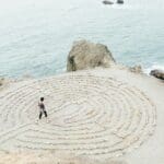 transformational travel image, featuring a person walking through a labyrinth next to a shoreline.