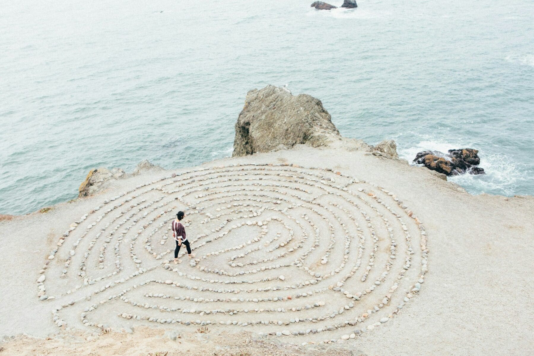 transformational travel image, featuring a person walking through a labyrinth next to a shoreline.